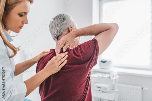 Caucasian female orthopedist examining senior male patient's back in clinic photo