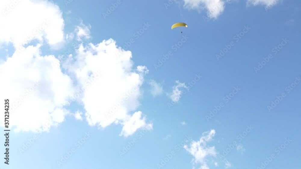Paraglider flying over fields in sunny day. Paraglider in the blue sky.  Silhouette of paraglide flying in the sky with clouds in a light of sunrise. Paraglider flying in the air stream.
