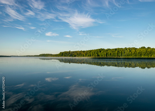 cloud reflections in clear and calm lake water, forest in the background, summer morning
