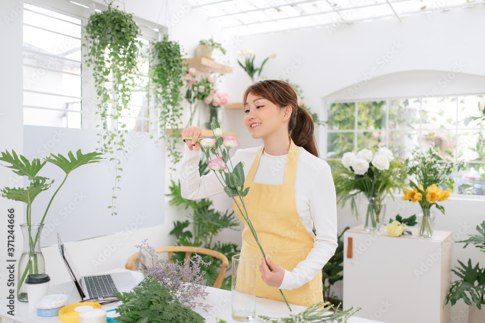 Female asian florist standing at a table in her flower workshop holding mixed flowers Female asian florist standing at a table in her flower workshop holding mixed flowers