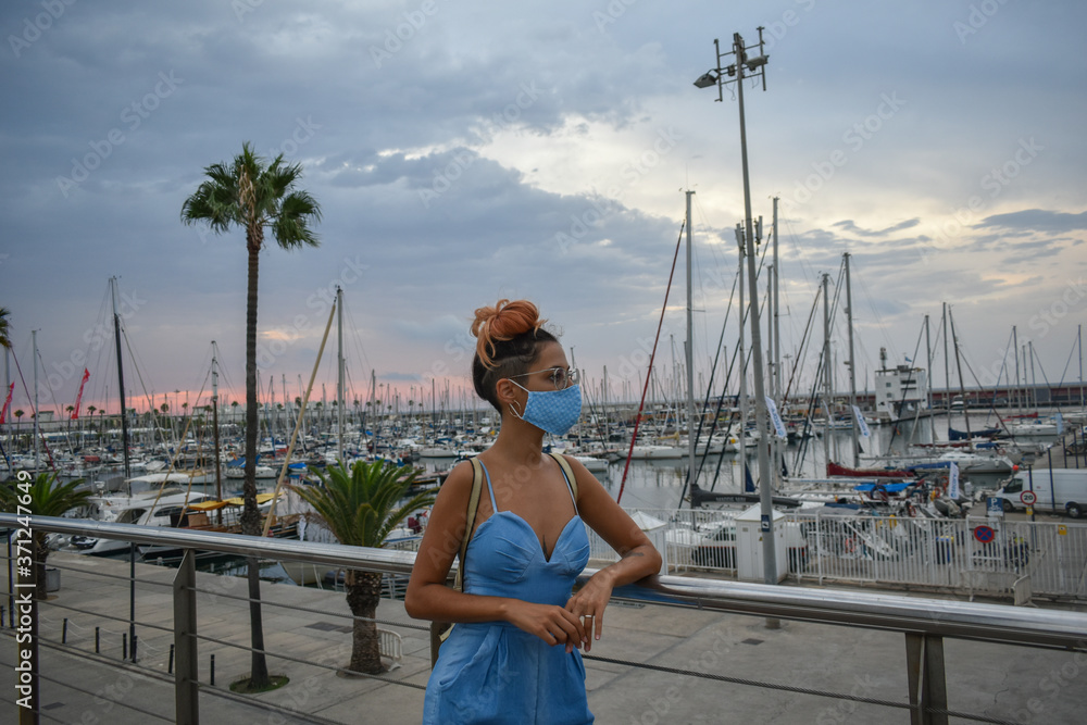 Woman standing in the port of Barcelona, ​​strolling wearing a mask to protect against the coronavirus
