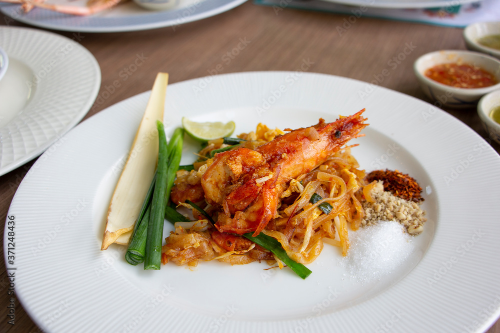 Fried noodles Pad Thai with prawn, piece of banana blossom and chive on white plate