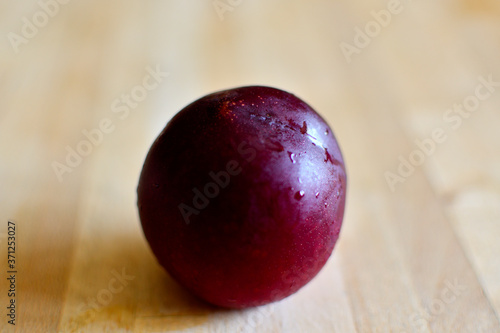 A plum on a wooden table covered with dew after being in the refrigerator.