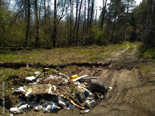 A huge mountain of household waste lies on the road in a green, blooming forest.