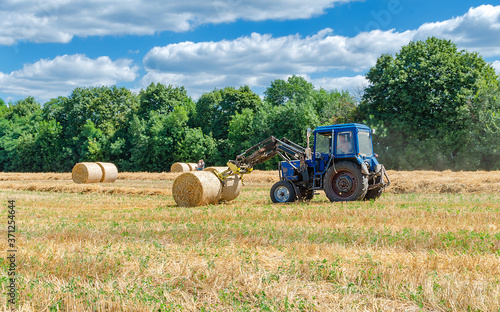 straw in round bales and a tractor in the field