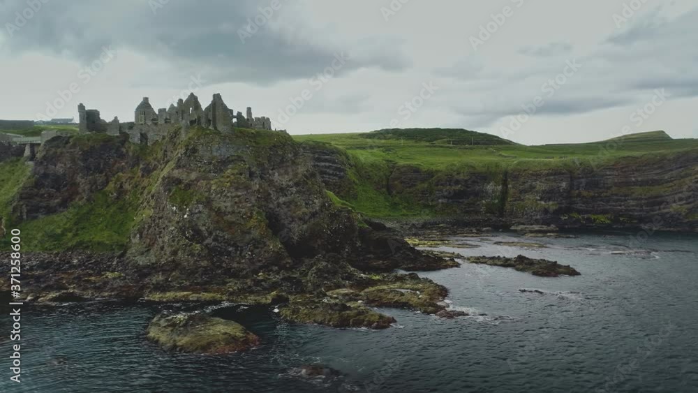 Ireland Dunluce castle ruins aerial shot on greenery basalt's cliff. Panning flight above fortress on seascape of ocean bay. Epic cinematic ancient building in Antrim Co. Footage view in 4K, UHD Ireland Dunluce castle ruins aerial shot on greenery basalt's cliff. Panning flight above fortress on seascape of ocean bay. Epic cinematic ancient building in Antrim Co. Footage view in 4K, UHD