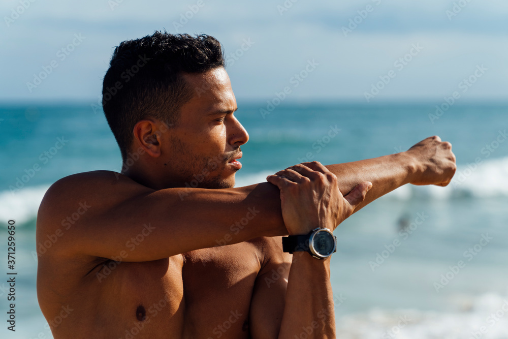 © HEX./Stocksy - Male Athlete Stretching After Sport Training on the Beach Close to the Sea. Front View with Large Copy Space
