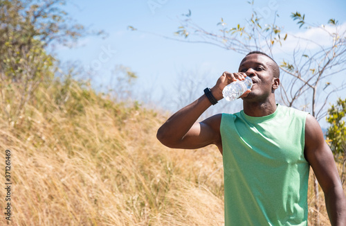 African Man drinking water from bottle after running outdoor. Forest and meadow background.