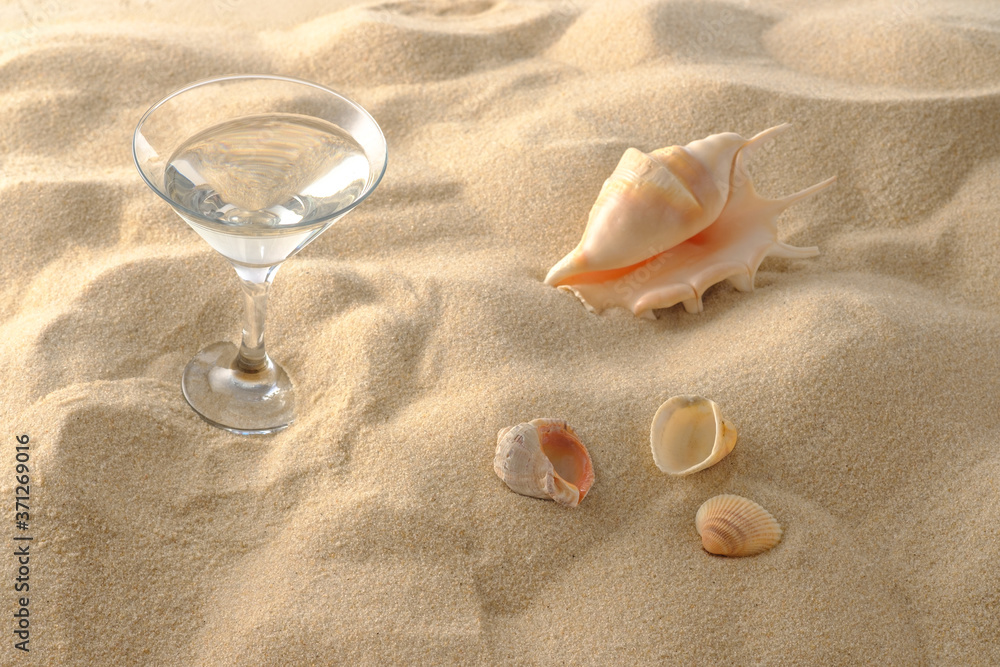 Beach vacation concept. Cool drinks on the beach sand. A glass of refreshing drink and seashell. Close-up.