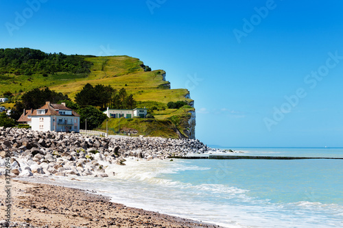 Etretat town beach and famous green grass cliffs over blue sky scenic view, France