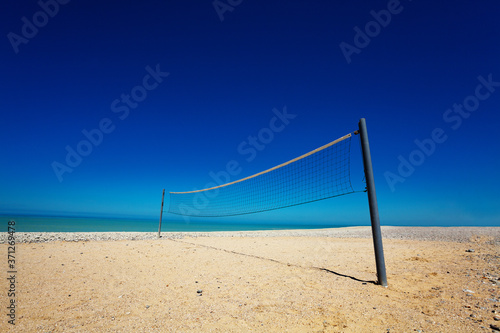Volleyball net over clean sand beach and ocean background with blue sky