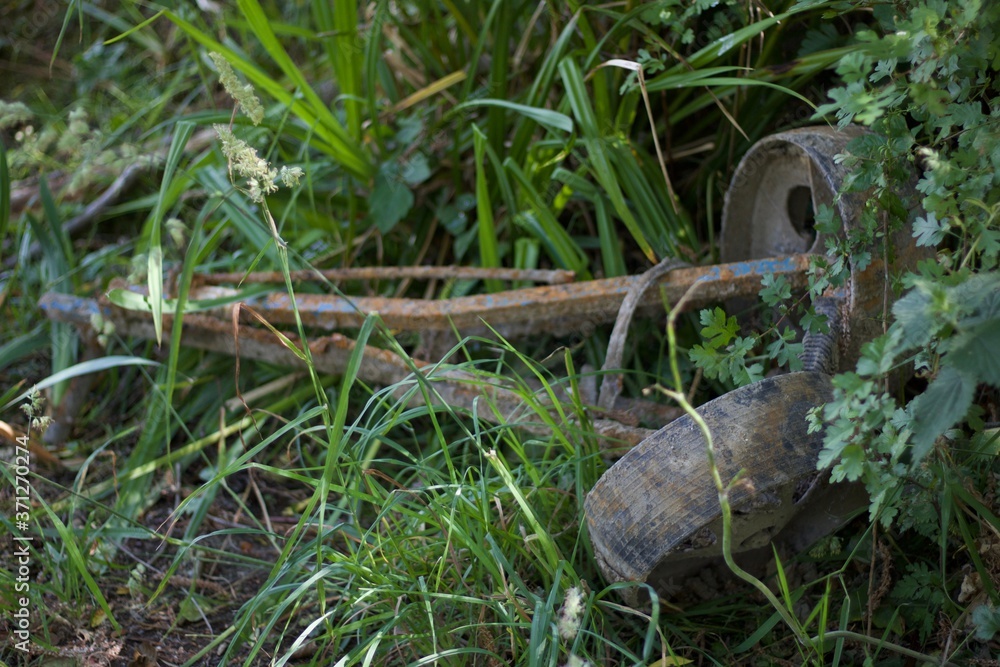 Fototapeta premium Rusted old gold trolley with wheels lying in grassy undergrowth