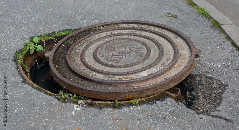 The rusty lid of an old sewer manhole has been pushed to the side