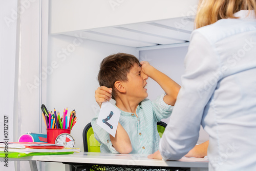 Boy with autism spectrum disorder show pain and negative expression while learning numbers sitting by teacher photo