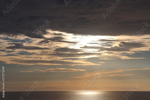 Gold twilight sky with clouds hiding the sun over a smooth glistening ocean © Fillmore