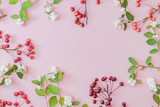 Flat lay autumn composition with green leaves, white berries and small red apples on a pink background