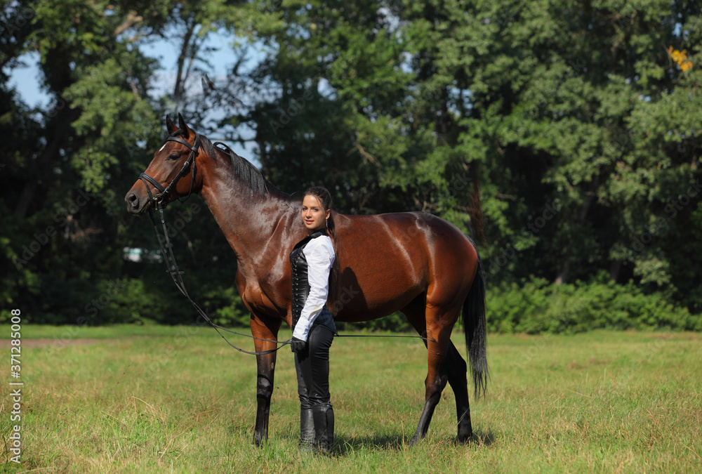Beautiful woman in a leather amazon suit walks with a horse in the field Beautiful woman in a leather amazon suit walks with a horse in the field