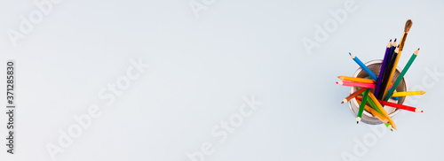 A set of colored bright pencils in a stand on a light gray background. Photo banner. View from above. Place for text.