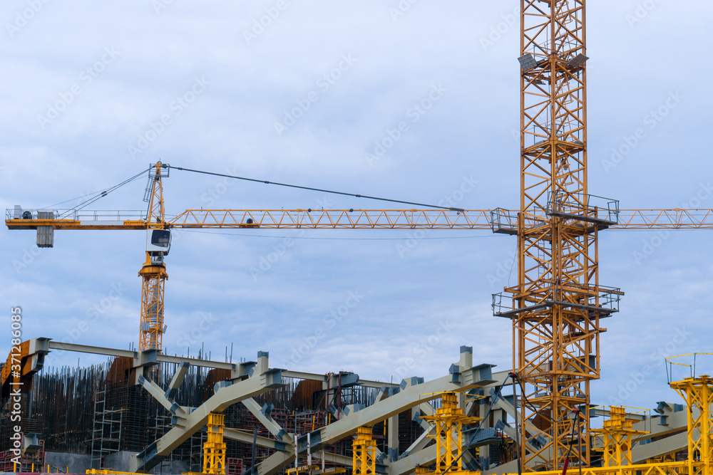 Industrial tower cranes at a construction site. Real estate construction. Cranes against the cloudy sky.