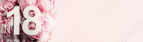 Creative layout. Peony flowers, digit eighteen. Birthday greeting card with inscription 18. Anniversary concept. Top view. Copy space. Stylish white numeral on flower background. Numerical digit