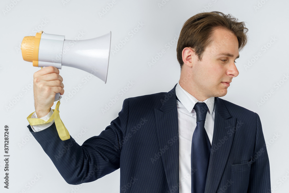 A businessman is holding a loudspeaker that is directed towards his face. White background. A businessman is holding a loudspeaker that is directed towards his face. White background.