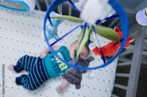 Φωτογραφία looking at a mobile toy in his crib and playmat