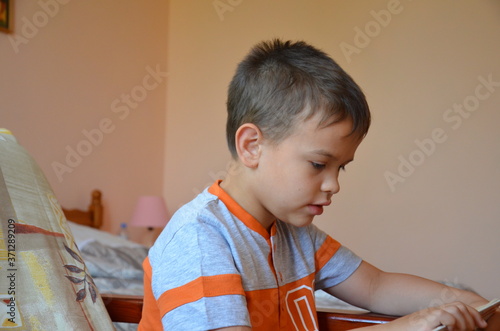boy reads a book sitting at home on an armchair in an orange t-shirt. study. hobby. Adventure. Young man reading a book