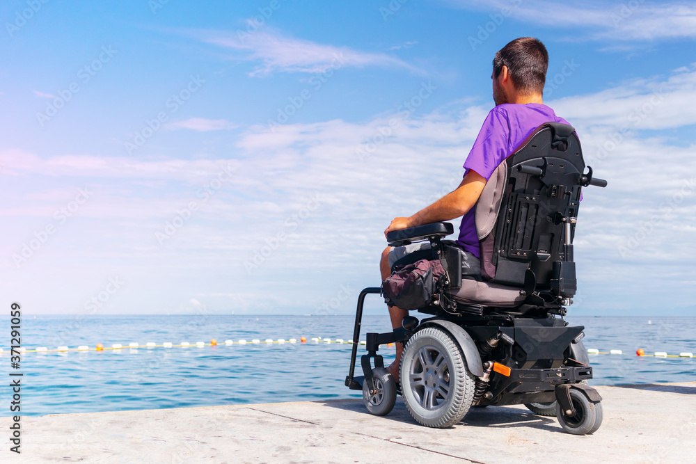 Man sitting in a wheelchair looking at sea. Head and spine injury. Dangers of jumping into water from heights. Man sitting in a wheelchair looking at sea. Head and spine injury. Dangers of jumping into water from heights.