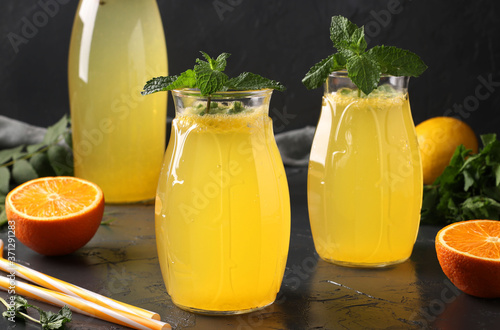 Homemade lemonade of lemons and oranges, decorated with mint in tall glasses with straws and a bottle in the background, Horizontal format