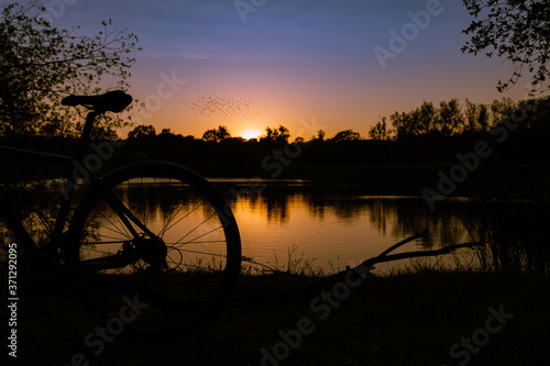 Bike stood next to a river at sunset as birds fly over