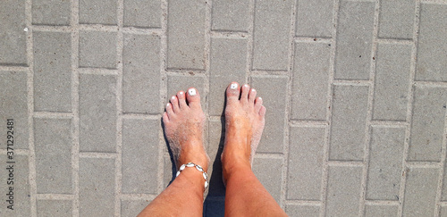 Canvas Print Tanned and sandy feet with white nail varnish and seashell anklet on the concret