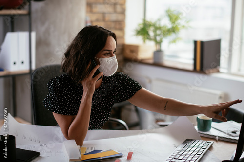 Beautiful businesswoman with medical mask working in office. Young businesswoman uing the phone. photo