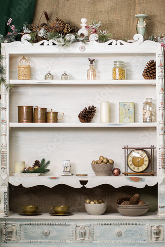 Stylish antique decor with pine cones. White cabinet with antiques on the shelves.
