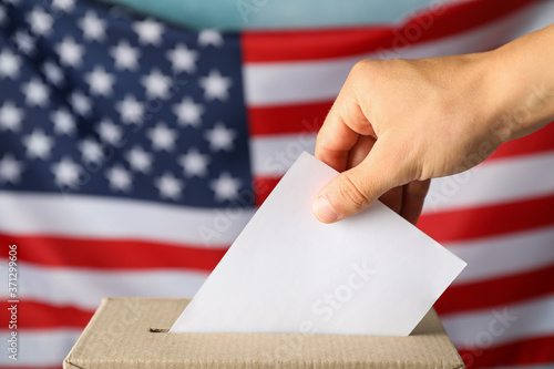 Man putting ballot into voting box against american flag