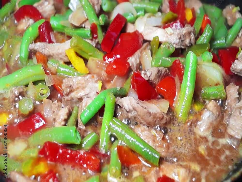 Frying vegetables with meat in a pan. Fry onions, bell peppers, green beans, chicken, pork and butter in the kitchen. Close-up. Asian cuisine. Frying vegetables with meat in a pan. Fry onions, bell peppers, green beans, chicken, pork and butter in the kitchen. Close-up. Asian cuisine.