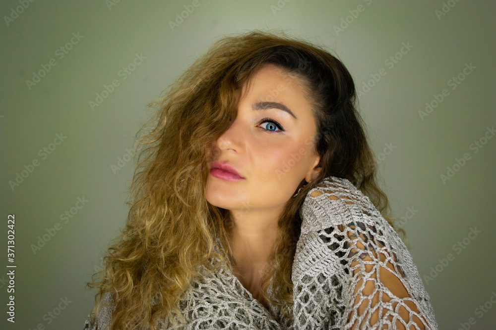 Half face portrait of a beautiful European blue eyed girl with curly dark hair on a green leaves background. Half face portrait of a beautiful European blue eyed girl with curly dark hair on a green leaves background.