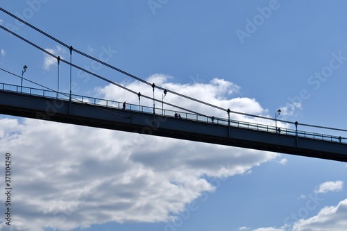 silhouette of footbridge on ropes on blurred background of blue sky with white clouds