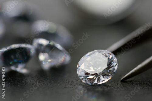 brilliant cut diamond held by tweezers on black background