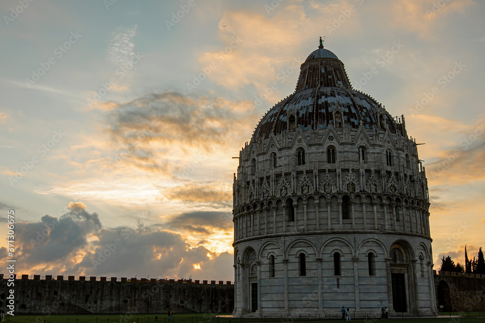 Isolated image of the Pisa Baptistery, a historic landmark and part of the world famous piazza del miracoli (cathedral square) in Pisa Tuscany at sunset with sun, clouds and walls in the background.