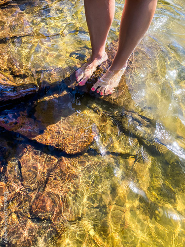 Young woman standing on rocks in water. Bare feet and legs with pink nailpolish. Karlstad, Värmland, Sweden.