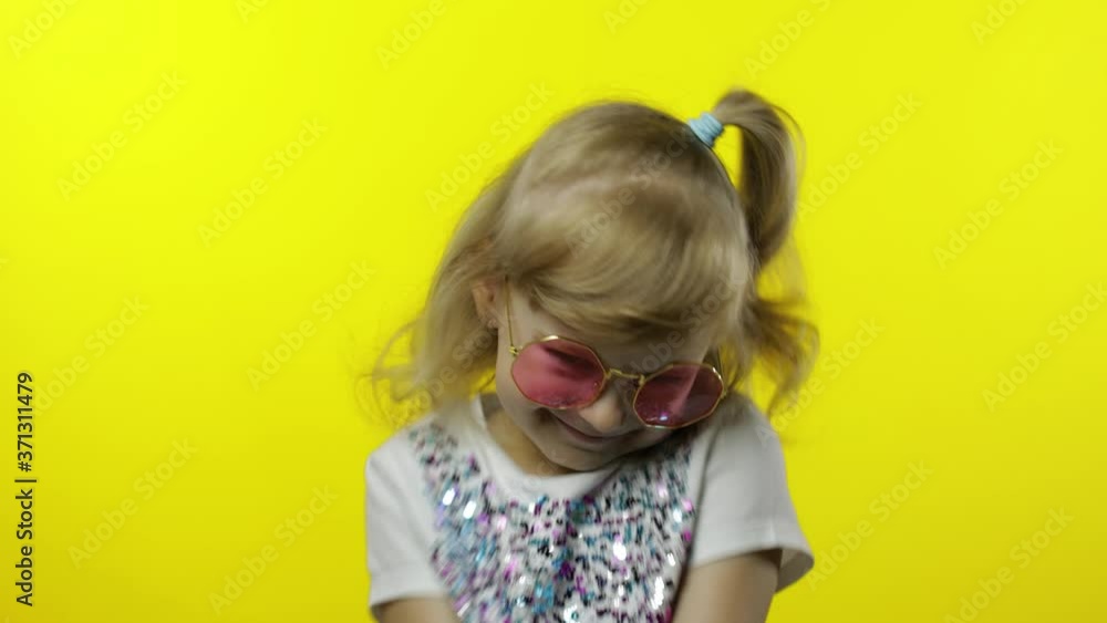 Child smiling, looking at camera. Girl tourist in pink sunglasses posing on yellow background Child smiling, looking at camera. Girl tourist in pink sunglasses posing on yellow background
