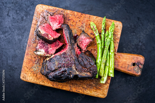Barbecue dry aged wagyu bistecca alla fiorentina beef steak sliced with large filet piece with green asparagus and red wine salt offered as top view on an old rustic wooden cutting board
