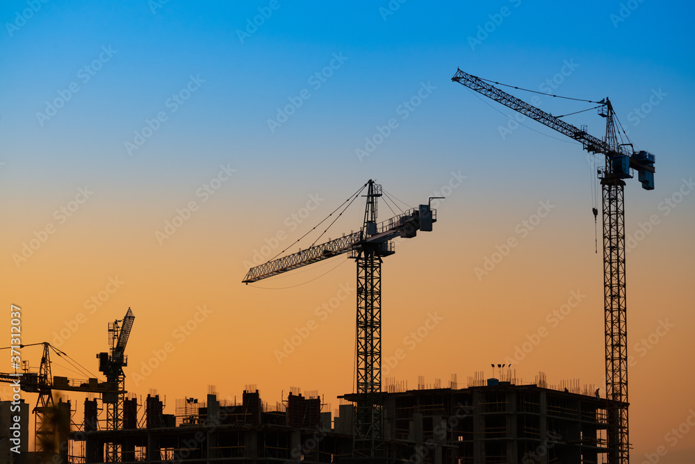 Big building crane on sunset blue and orange sky background