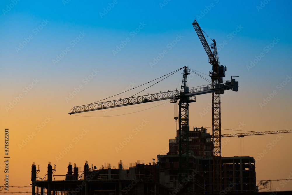 Big building crane on sunset blue and orange sky background