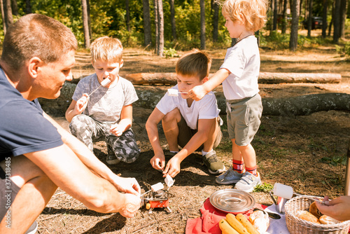 Three little boys staged a halt with a tent and a campfire in the woods in summer sunny day.campfire food