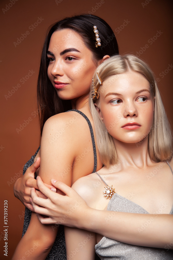 two pretty diverse girls happy posing together: blond and brunette on brown background, lifestyle people concept two pretty diverse girls happy posing together: blond and brunette on brown background, lifestyle people concept