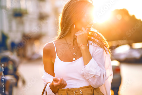 Sensual summer sunny portrait of elegant hipster blogger woman wearing minimalistic casual outfit  clear glasses and gold accessories  powerful sunlight.