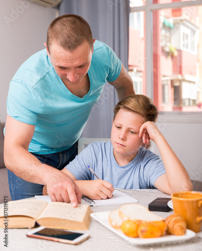 Man with his adult son are reading book together for homework at the home.