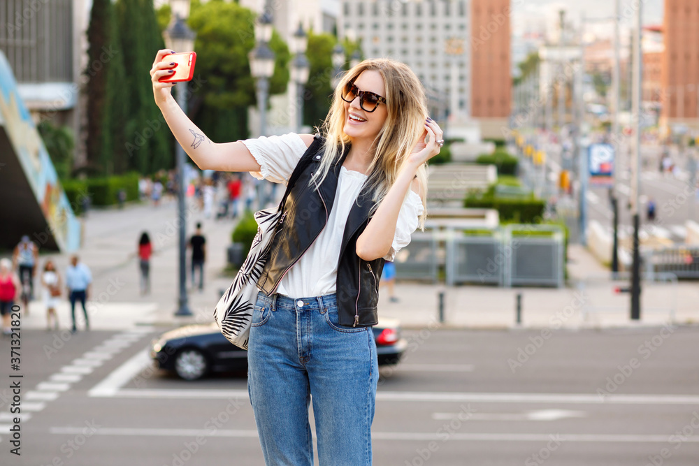 Pretty tourist blonde woman making selfie on the street, stylish casual outfit and sunglasses, traveling in Europe.