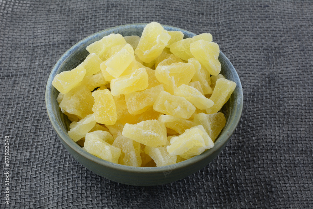 Dried soft dehydrated pineapple chunks in ceramic snack bowl on burlap tablecloth